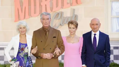 PA Media Helen Mirren in a blue dress and white jacket, Pierce Brosnan in a brown suit, shirt and tie, Celia Imrie in a pink dress and Sir Ben Kingsley in a blue suit, white shirt and purple tie. All at looking forward and smiling.