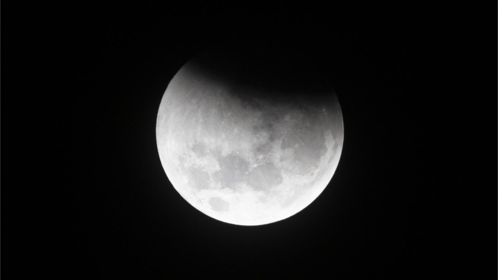 An image of a full moon pictured during an eclipse, hanging against a black sky. The top edge of the lunar disk is hidden by Earth's shadow.