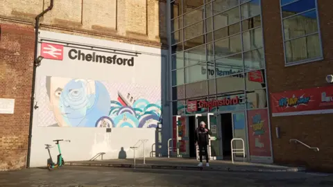 Owen Ward/BBC The Chelmsford railway station entrance in the morning sunlight. A mural is painted on the station viaduct, which depicts a man, waves and the Titanic ship. It is inspired by the Marconi inventor and his telegraph system used on the ship.