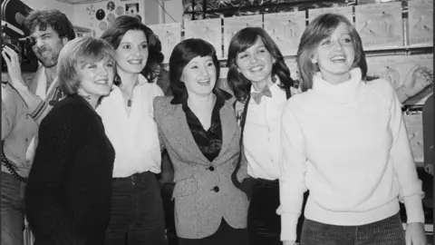 PA Media A black and white photo of the five smiling Nolan sisters in 1978 as they arrive at a record shop to sign copies for fans