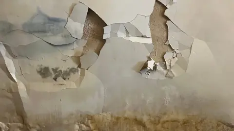 BBC A bedroom wall in Luton covered in black mould and damp. The plaster is cracked and falling off the wall. This is one of more than 30,000 homes the government says have had poorly-installed insulation since 2022.