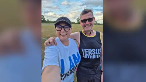 Handout A selfie of Dave and Becky on a field close to a running track.