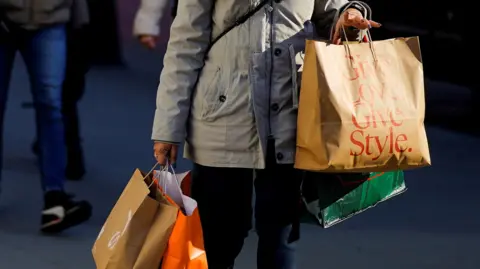 Reuters A woman stands on the street holding several shopping bags.