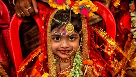 LightRocket via Getty Images A young girl in a bright red and gold outfit is seen posing for a photo during Durga puja festivities at the Adyapith temple.