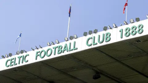 PA Media The top of the Celtic Park stadium, with flags on the roof and a green sign which reads Celtic Football Club 1888