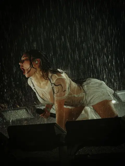 Pupat Chenaksara Charli XCX in a white, short outfit on all fours being showered with water on stage