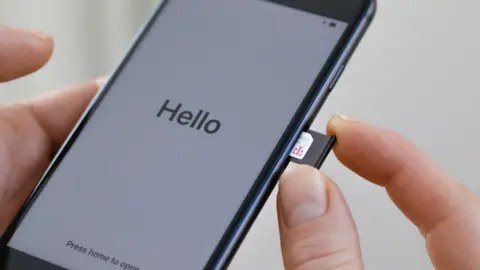 Getty Images A person pushing a sim card into a mobile phone. On the mobile screen, it says 'Hello'