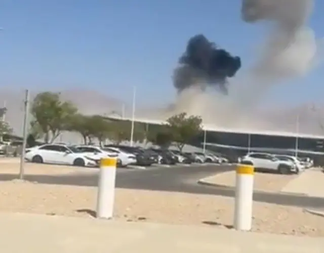 Smoke rising from above an airport with a car park in front