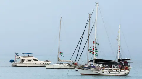 EPA Three sailing boats are seen anchored in turquoise waters, with Palestinian flags strung through the rigging and masts of the vessels.