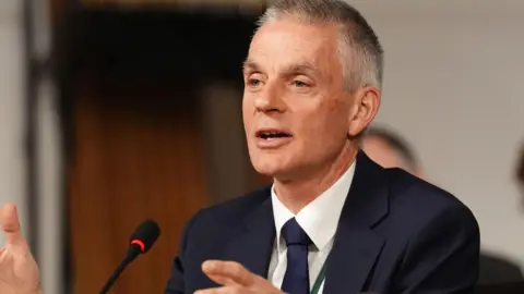 PA Tim Davie wearing a navy blue suit, navy tie and white shirt