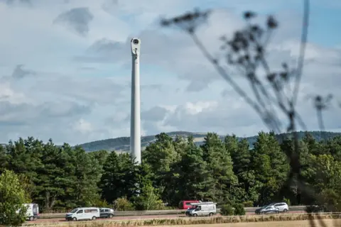 The remains of a wind turbine in a field with traffic in the foreground
