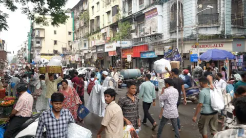 Vishnu Vardhan A busy street scene with roadside vendors and cloth merchants carrying their goods in Mumbai's Crawford market area.