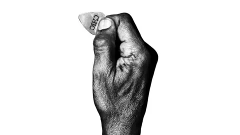 Platon A black and white picture of Nile Rodgers' hand holding a plectrum