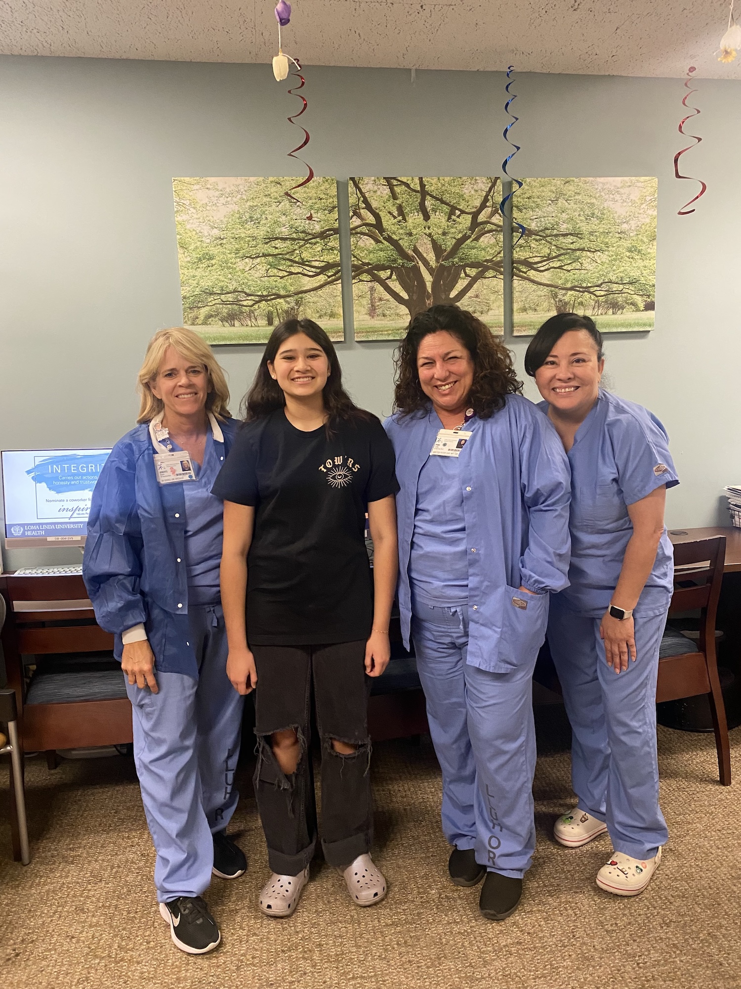 A young patient in all black stands with three nurses in blue scrubs