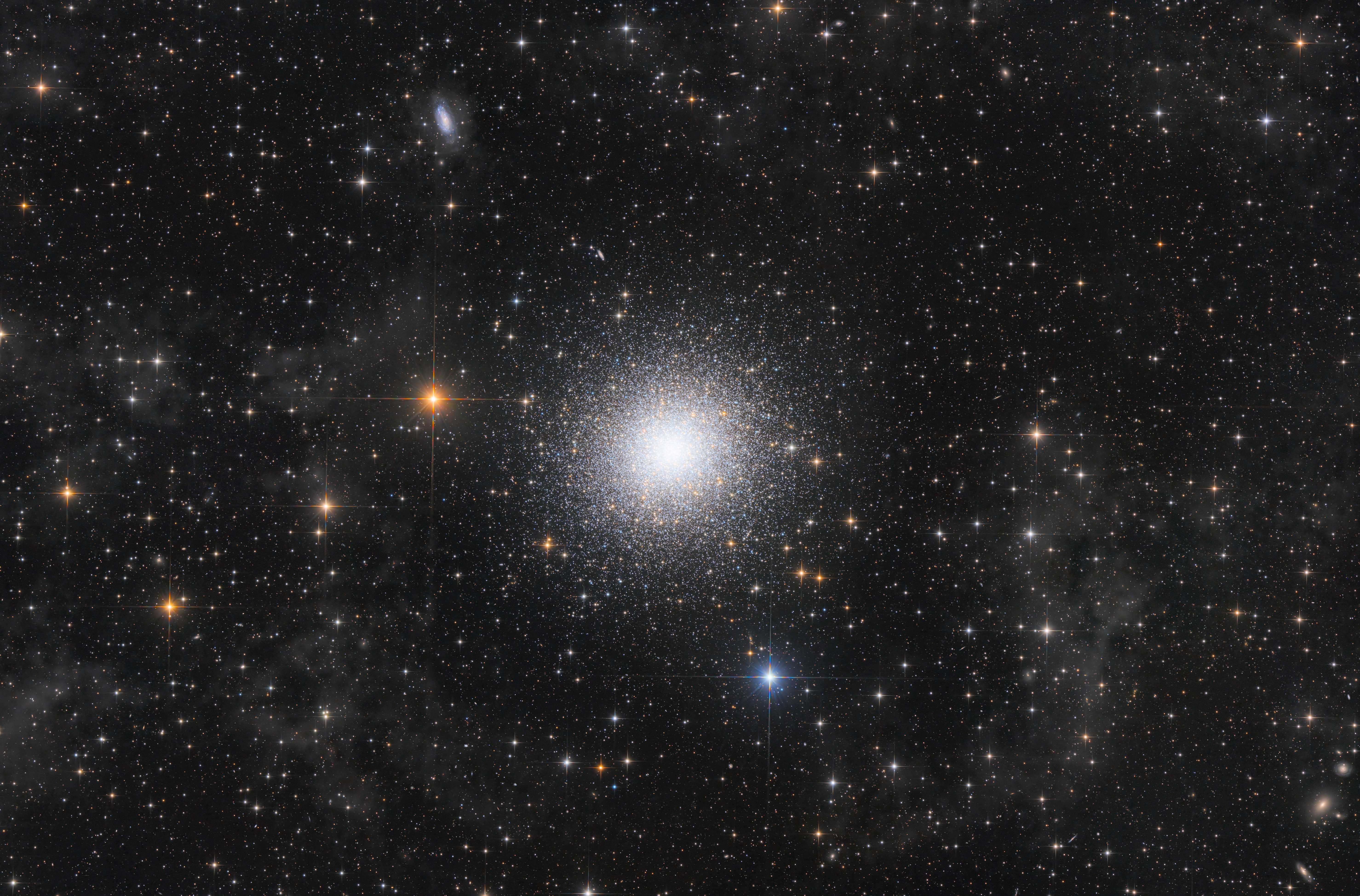 A dense cluster of stars is pictured at the centre of an image against a dark sky studded with multi coloured stellar bodies.