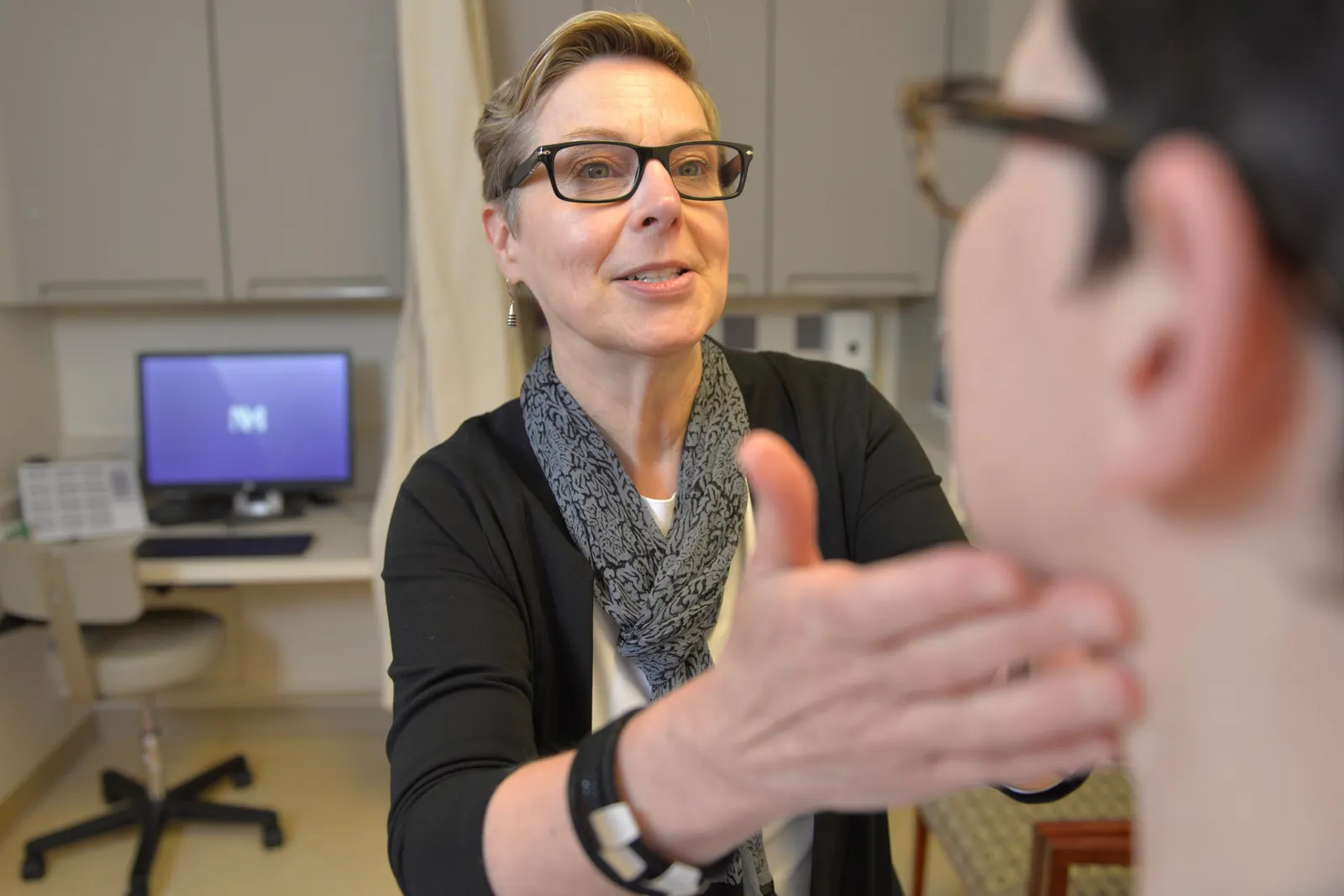 A person feels the under jaw of another person in a doctor's exam room.