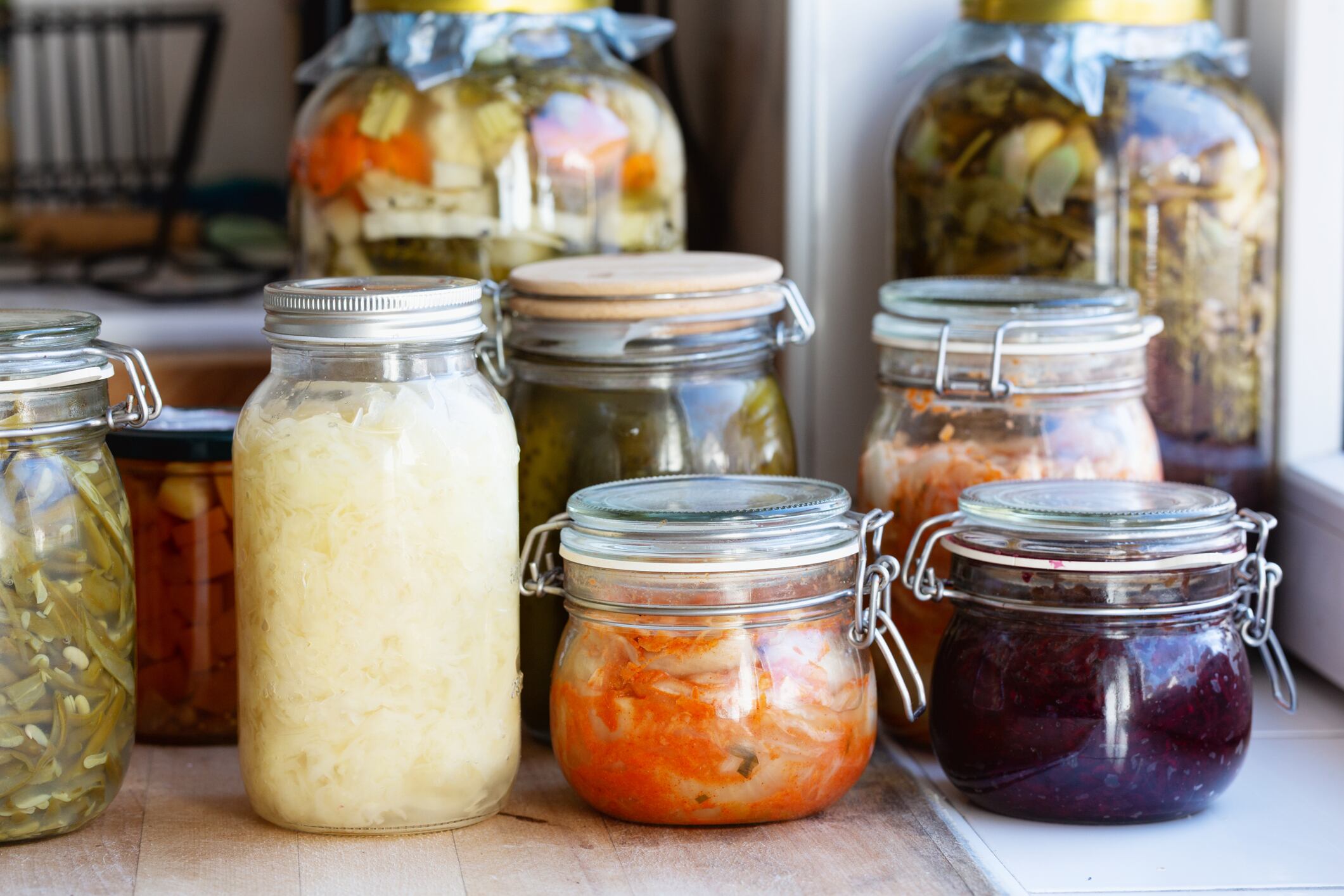 Jars with a varation of fermented vegetables in jars such as sauerkraut, green beans,beet,cucumber and kimchee at on a wooden board in kitchen