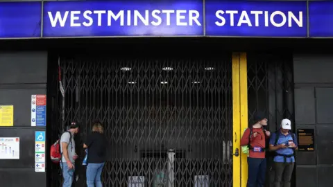 EPA Westminster Tube station with its shutter closed and people standing outside it.