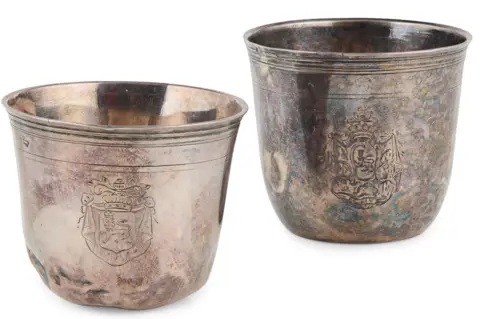 LYON & TURNBULL The beakers are cup-shaped and have coats of arms and heraldic crests engraved on the outside.