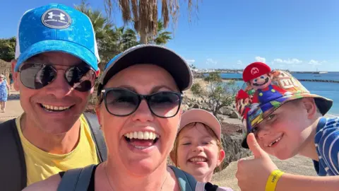 Gemma Botting Matt, Gemma and their children smiling at the camera while on holiday together. A beach is behind them.