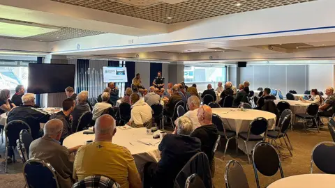BRFC Trust The weekly group showing mainly men over 50 years of age sitting at round tables listening to a guest speaker.