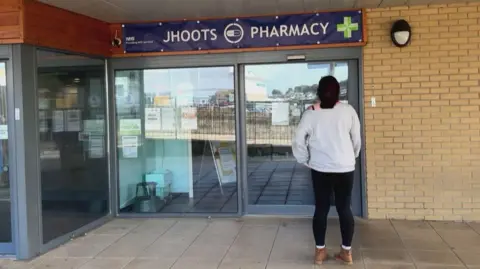 BBC A woman with her back to the camera standing on a precinct outside a closed JHoots branch, looking in the window.