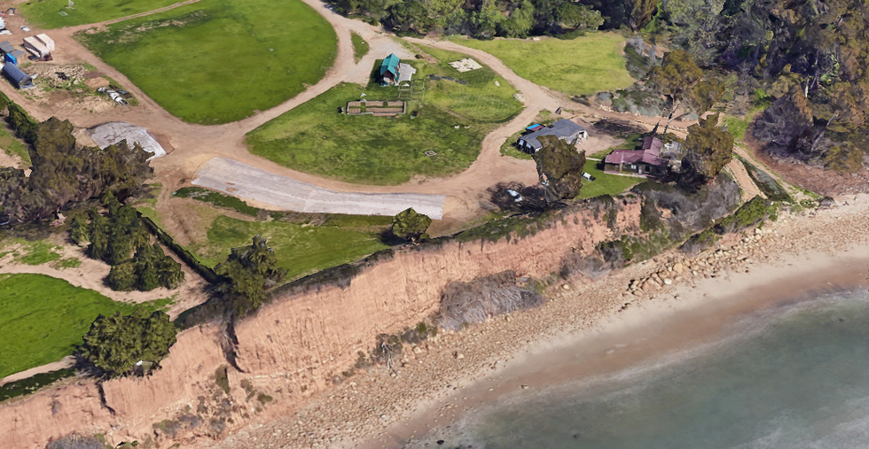 Aerial view of a coastal landscape featuring a cliff  grassy areas  and several buildings