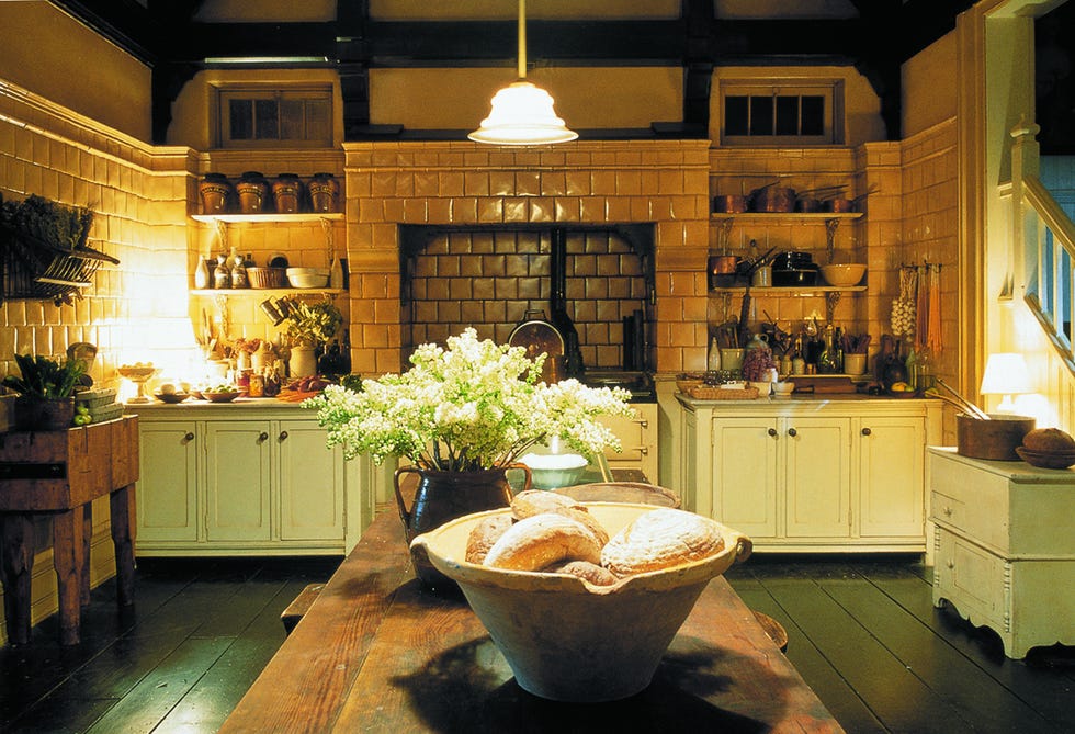 Rustic kitchen showcasing wooden table with bread and flowers, tiled walls, and various kitchenware.