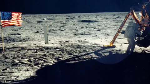 NASA One of the very few pictures of Neil Armstrong on the lunar surface. He is in his white astronaut suit with the lunar lander at the right of the frame. On the left is the US flag as the only colourful object in an otherwise bleak lunar landscape.