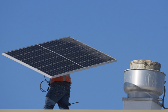 A worker carries a solar panel on the roof of the Alta Sea building, an urban, ocean-based research and blue technology innovation campus, at Berth 58 in the Port of Los Angeles on Sept. 4. [AP/YONHAP]