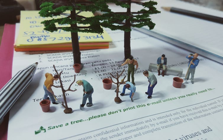 Plastic figures plant trees on top of paper saying 'please don't print'