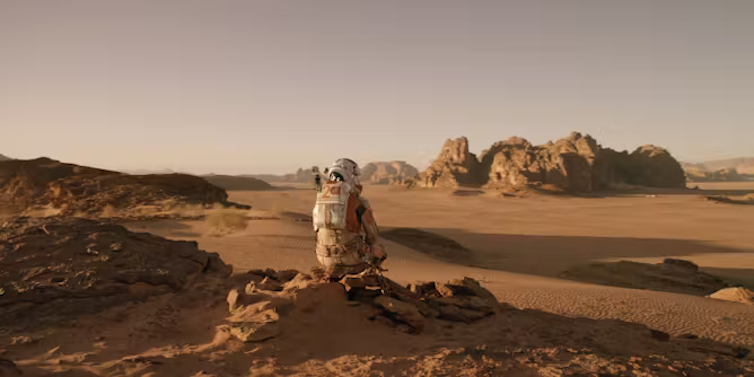 'The Martian' protagonist Mark Watney, donning a space suit, overlooks a Mars-scape.