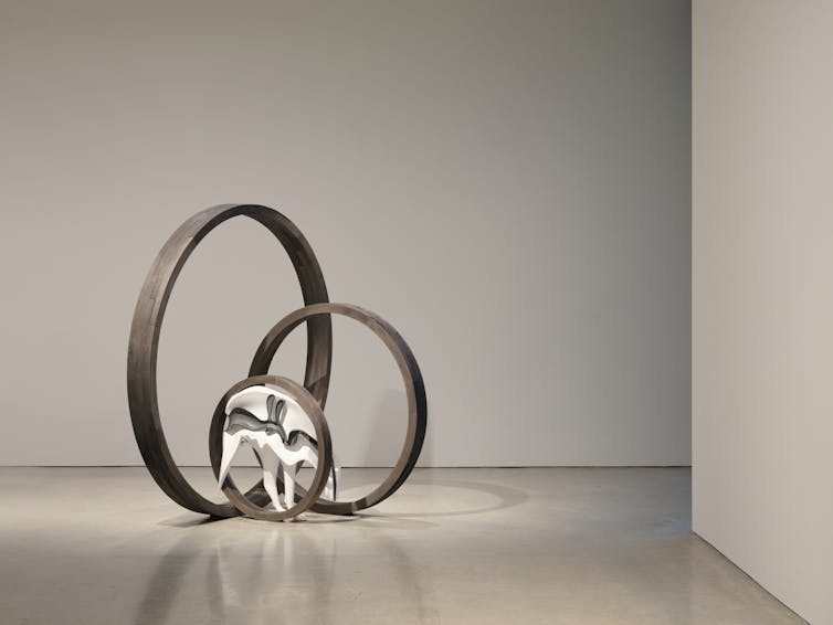 Metal sculpture featuring three intersecting silver rings and white dog