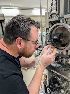 A man wearing glasses peering into a scientific instrument.