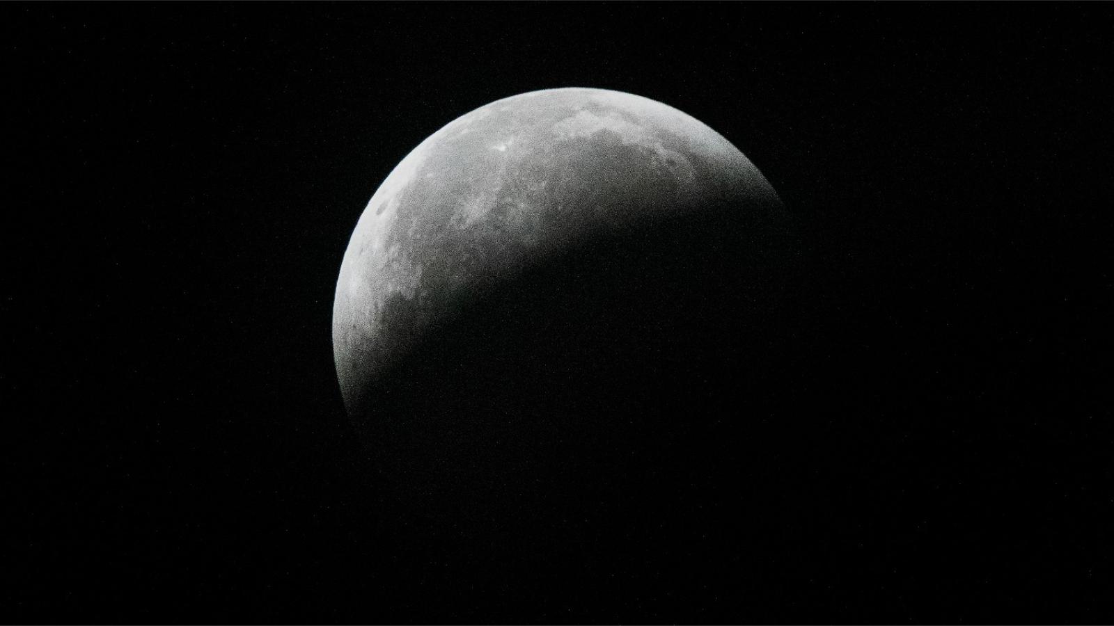 A full moon is pictured against a black sky. It's lower half is entirely hidden by Earth's curved shadow and dark basaltic plains called lunar maria can be seen marking the middle of the lunar disk.