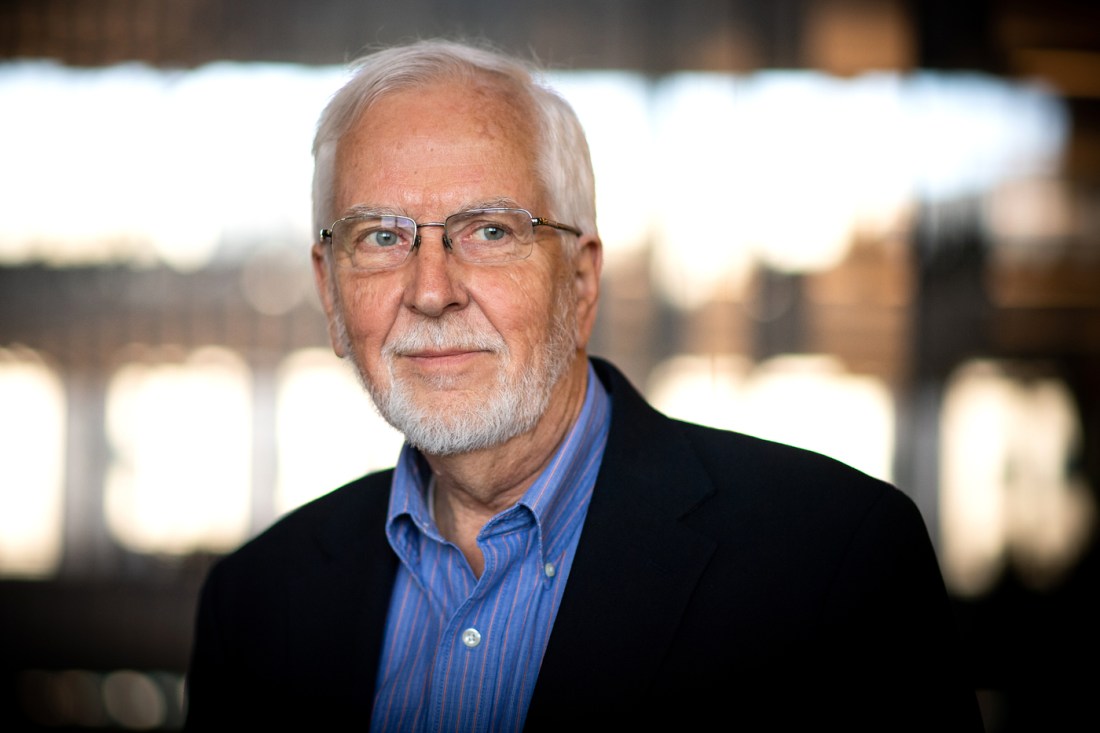 John Kwoka, a professor of economics, featured in a portrait with a neutral expression against a sleek background.