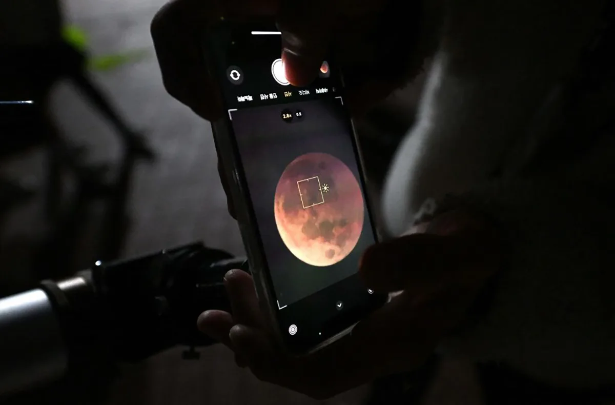 A man uses a smartphone to take picture of a blood moon through telescope during a total lunar eclipse in Goyang, northwest of Seoul, on November 8, 2022. (Photo by JUNG YEON-JE / AFP) (Photo by JUNG YEON-JE/AFP via Getty Images