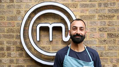 A portrait image of a contestant stood against an exposed brick wall, with the MasterChef circular white logo behind him.