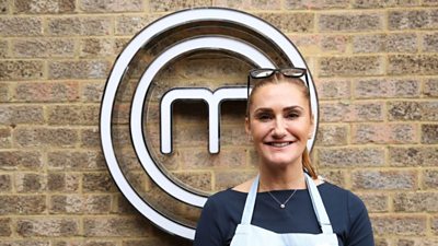 A portrait image of a contestant stood against an exposed brick wall, with the MasterChef circular white logo behind her.