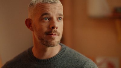 Russell Tovey as Guy looking at something off camera. Russell is wearing a dark grey jumper