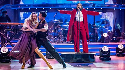 Strictly professional dancers Luba Mushtuk and Gorka Marquez perform together in front of Jessie J, who stands on a podium singing in a red suit with her arms wide open