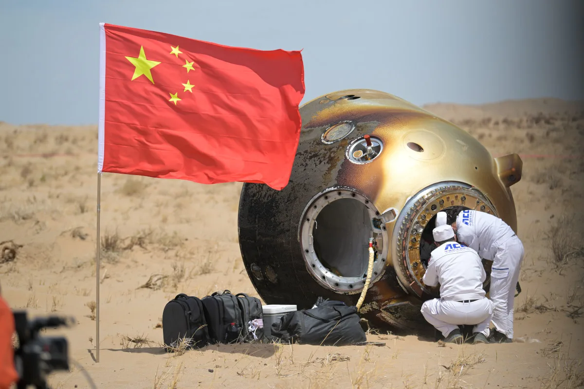 Photo of crew helping astronauts out of a spacecraft capsule in China, the Chinese flag is prominent in the foreground