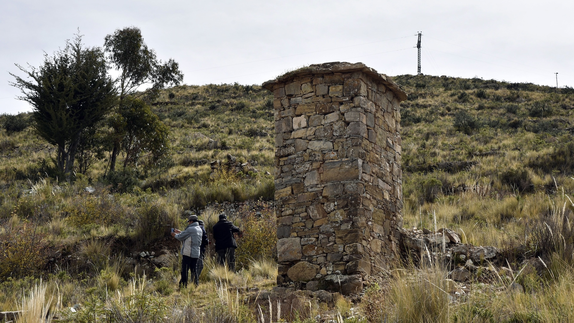 two people stand next to a small stone tower on a a dry grassy hill