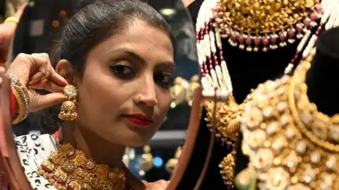 Getty Images A woman looks into the mirror as she tries on an earring in a jewellery shop in India.
