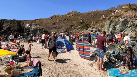 BBC A beach with lots of people and wind breaks, with cliffs behind and blue sea