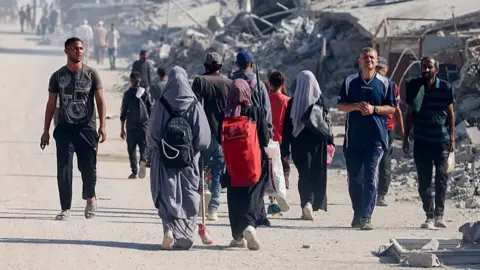 Getty Images Various people walking along in Gaza, mainly away from the camera, with huge piles of debris in the background.