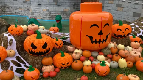 BBC A giant orange pumpkin sits on grass outside a castle at LEGOLAND surrounded by some smaller, real orange, yellow and red pumpkins, as well as some Lego ones