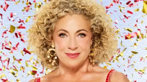 BBC Alex Kingston in tassled red dress with red and gold confetti falling behind her in a Strictly promotional photo