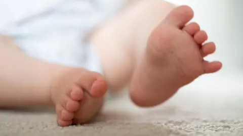 PA Media Close-up of two small bare feet resting on a soft, light-colored surface, with toes slightly curled and background softly blurred