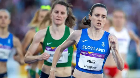 Getty Images A woman with a blue top saying Scotland and an athletics bib saying Muir is running around an athletics track. Several other female athletes can be seen following her in the background.